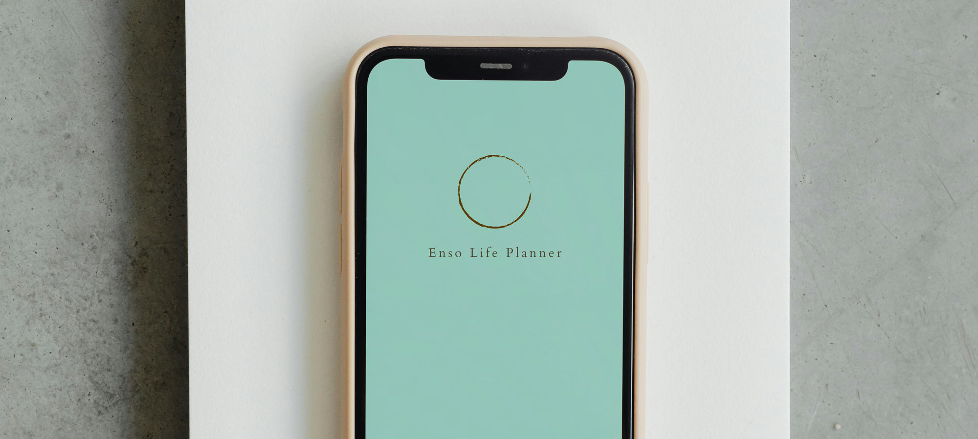 Enso Life Planner on phone screen that sits top of a blank notebook on a concrete surface